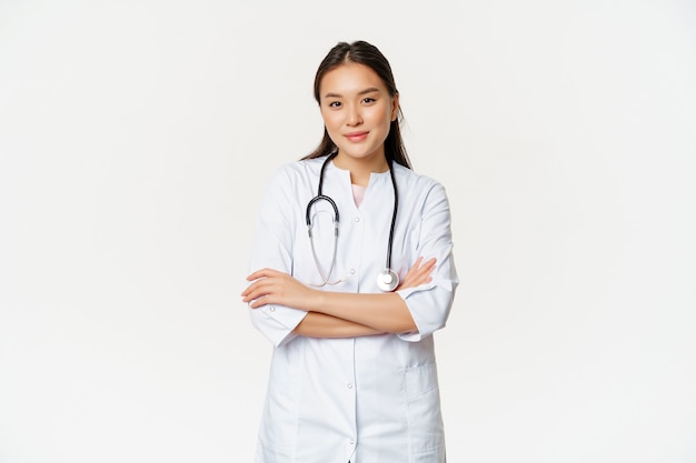 Immagine della dottoressa fiduciosa, stagista con stetoscopio e vestaglia medica, braccia incrociate come professionista, guardando fiducioso alla macchina fotografica, sfondo bianco