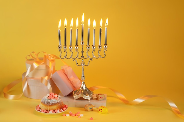 Immagine della festa ebraica Hanukkah con menorah tradizionali ciambelle candelabri e dreidels in legno trottola monete di cioccolato su sfondo giallo