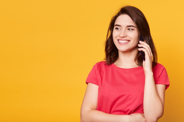 Immagine della giovane donna in maglietta casuale rossa che parla sulla conversazione di conduzione del telefono cellulare