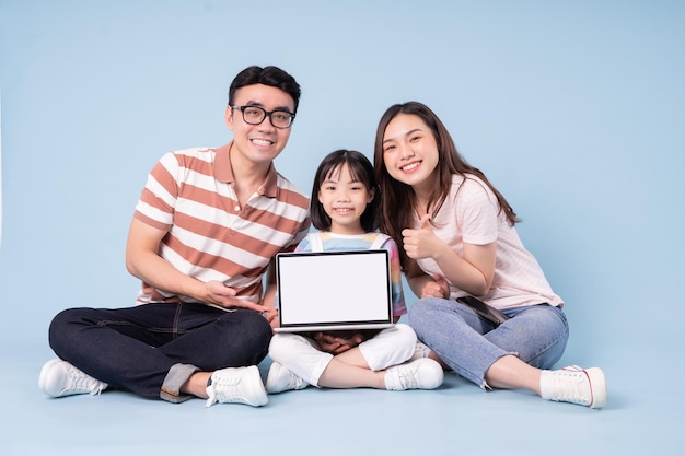 Immagine della giovane famiglia asiatica che utilizza il computer portatile su sfondo blu