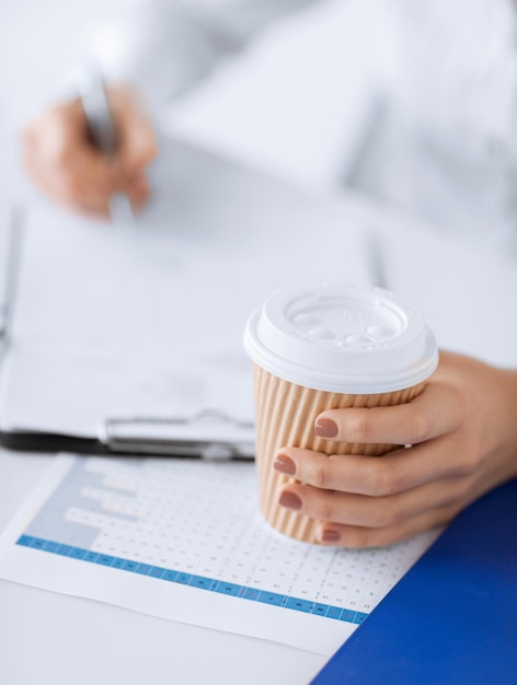immagine della mano di una donna che riempie carta bianca e beve caffè