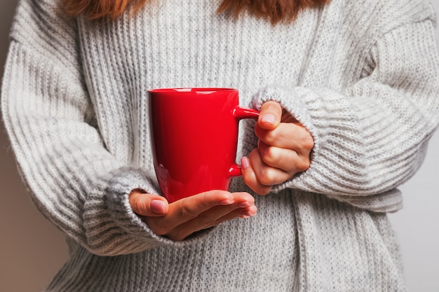 Immagine della mano di una donna che tiene una tazza da caffè rossa