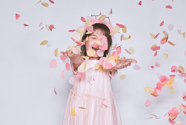 Immagine dello studio della bambina felice che indossa un abito rosa con la corona della principessa sulla testa isolata su sfondo bianco goditi la sorpresa dei coriandoli Ragazza sorridente giocosa che celebra la sua festa di compleanno divertendosi