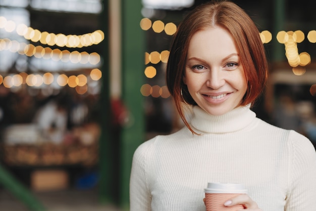 Immagine di attraente giovane donna con i capelli castani, dolce sorriso, indossa maglione dolcevita bianco