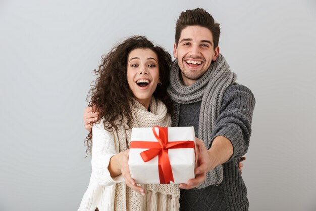 Immagine di bell'uomo e donna che si rallegrano stando in piedi con la scatola presente, isolata sopra il muro grigio