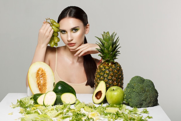 Immagine di bella giovane donna castana con la frutta e le verdure sulla tavola