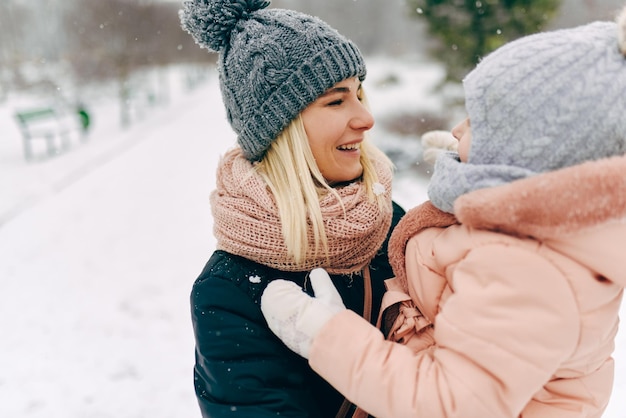 Immagine di bella madre felice che tiene il suo bambino sorridente ampiamente durante le passeggiate nel parco in un giorno di nevicata Giovane donna e sua figlia Atmosfera natalizia Ritratto di famiglia Maternità e infanzia