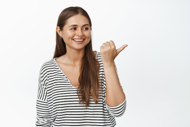 Immagine di candida donna felice che punta il dito e guarda a destra la pubblicità sorridente e ridente su sfondo bianco banner logo