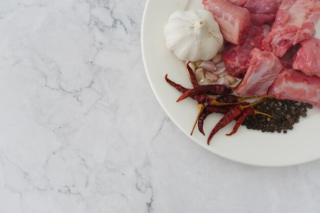 Immagine di carne cruda aglio pepe e peperoncini secchi in un piatto bianco su sfondo bianco