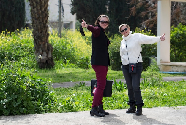 Immagine di due donne adulte eccitate che mostrano i pollici in su mentre posano sulla strada della città. Sorride felice