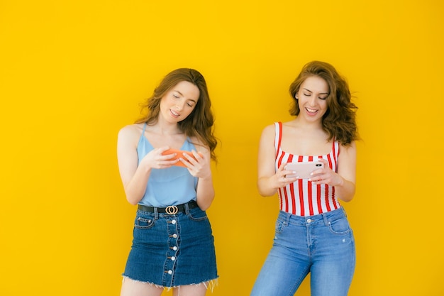 Immagine di due giovani belle ragazze che indossano magliette divertendosi e giocando ai videogiochi sul cellulare