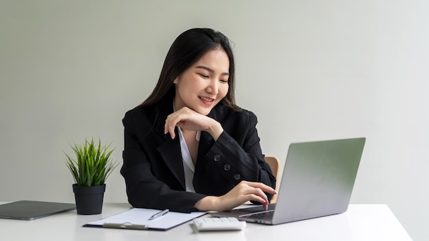 Immagine di felice sorridente imprenditrice asiatica che lavora sul suo computer portatile in ufficio.