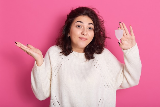 Immagine di giovane donna castana con capelli ondulati che tengono tazza mestruale