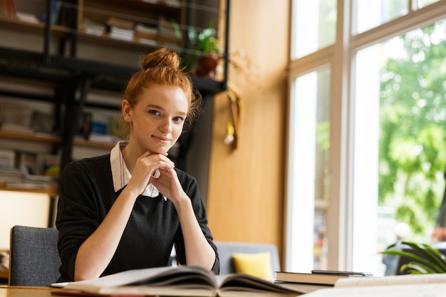 Immagine di giovane donna caucasica studiando, mentre è seduto alla scrivania in biblioteca universitaria con parete da scaffale