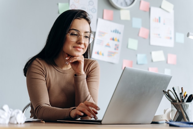 Immagine di giovane donna d'affari felice, felice, bella sedersi al chiuso in ufficio utilizzando il computer portatile