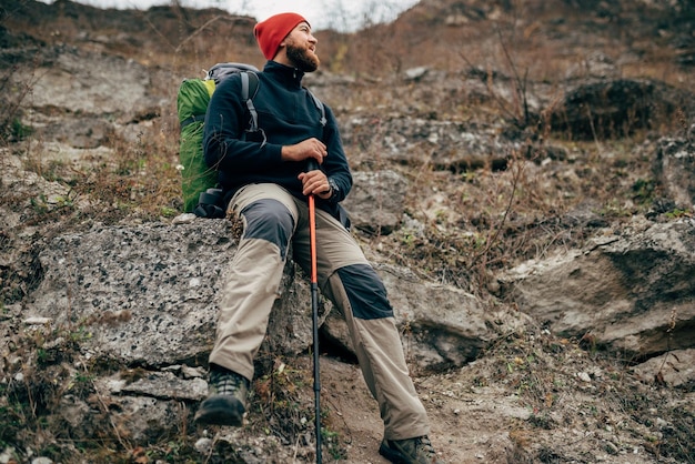 Immagine di giovane escursionista felice con cappello verde sentirsi bene dopo le escursioni in montagna Maschio barbuto viaggiatore sorridente e sentirsi felice durante il trekking nel suo viaggio Stile di vita di viaggio