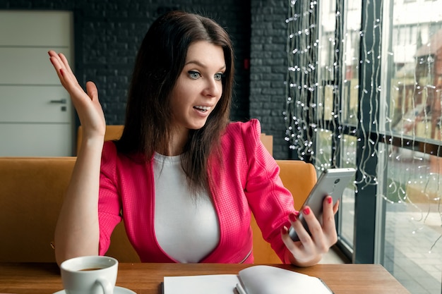 Immagine di giovane scioccato eccitato donna d'affari seduto in casa utilizzando il telefono cellulare