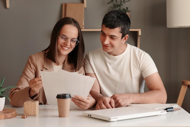 Immagine di giovani avvocati aziendali che modificano il testo del nuovo contratto utilizzando un computer portatile seduto al tavolo con un notebook in un ufficio moderno che esprime emozioni positive godendo di lavorare insieme