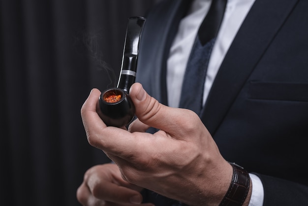 Immagine di mani maschili che tengono una pipa. Il fumo di tabacco concetto. Tecnica mista