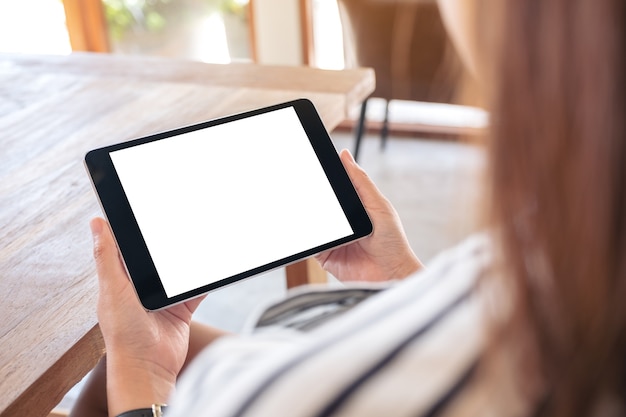 Immagine di mockup di una donna seduta e che tiene un tablet pc nero con lo schermo del desktop bianco vuoto orizzontalmente