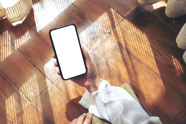 Immagine di mockup vista dall'alto di una donna che tiene e utilizza il telefono cellulare nero con lo schermo del desktop vuoto mentre si sdraia sul pavimento con una sensazione di relax