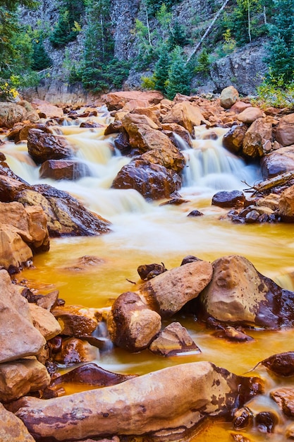 Immagine di pietre rosse lungo il fiume dorato con cascate