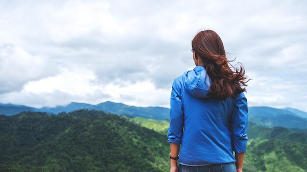 Immagine di retrovisione del viaggiatore femminile che esamina una bella vista sulle montagne verdi