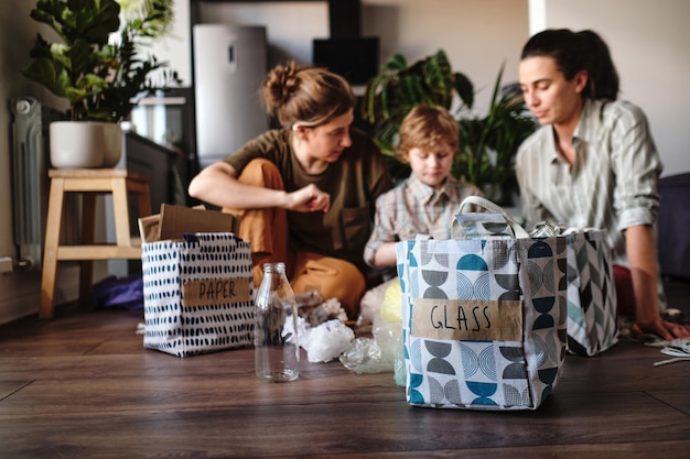 Immagine di sacchi ordinati con rifiuti diversi che si preparano per il riciclaggio con la famiglia seduta sullo sfondo