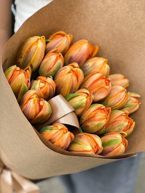 Immagine di sfondo di bellissimi fiori in primo piano. Un bouquet di tulipani arancioni di un'insolita varietà di carta artigianale per un regalo di lusso per una vacanza. Piante delicate in un negozio di fiori