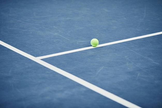 Immagine di sfondo minima di una singola pallina da tennis gialla su pavimento blu nello spazio di copia del campo da tennis