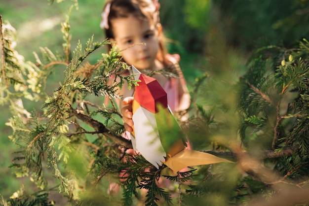 Immagine di uccello di carta colorato e bambina carina sfocata che gioca nel parco Adorabile bambino che gioca con un giocattolo all'aperto Ambiente ecologico Bambino che impara a prendersi cura e proteggere la natura