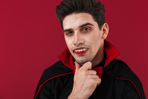 Immagine di un attraente vampiro con sangue e zanne in costume nero di halloween