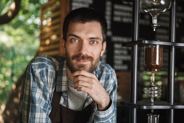 Immagine di un barista soddisfatto che indossa un grembiule che fa il caffè mentre lavora al bar o al caffè all'aperto