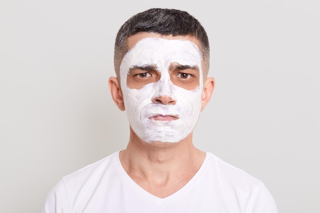 Immagine di un bell'uomo sconvolto e offeso con maschera di cosmetologia di ringiovanimento che esegue procedure cosmetiche guardando la fotocamera con labbra imbronciate che esprimono dolore