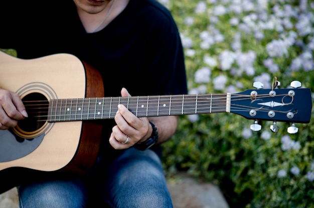 Immagine di un chitarrista, un giovane che gioca una chitarra mentre sedendosi in un giardino naturale, concetto di musica