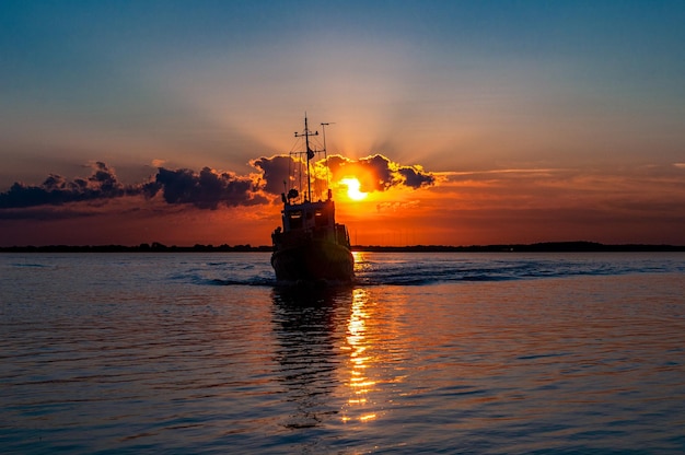 Immagine di un fiume al tramonto con una piccola barca drammatica nuvole e riflesso del sole sull'acqua