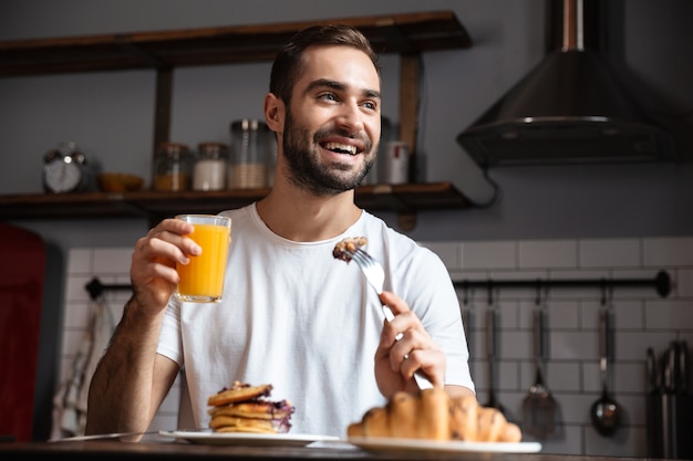 Immagine di un giovane ragazzo di 30 anni seduto a tavola e mangiare cibo mentre si fa colazione in un appartamento moderno