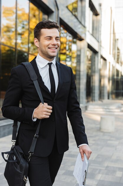 Immagine di un giovane uomo d'affari bello felice camminare all'aperto vicino al centro business con appunti.