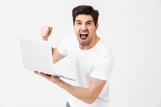 Immagine di un giovane urlante scioccato in posa isolata su un muro bianco utilizzando un computer portatile.