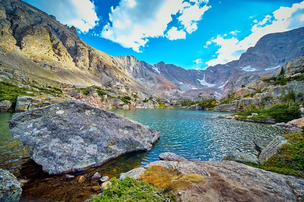 Immagine di un grande masso di licheni che riposa nel lago circondato da montagne rocciose