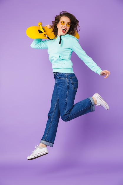 Immagine di un'incredibile giovane donna felice in posa isolata sopra la parete viola della holding dello skateboard.