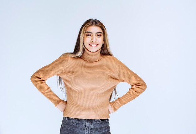 Immagine di un modello di giovane donna in maglione marrone in piedi con le mani sui fianchi.