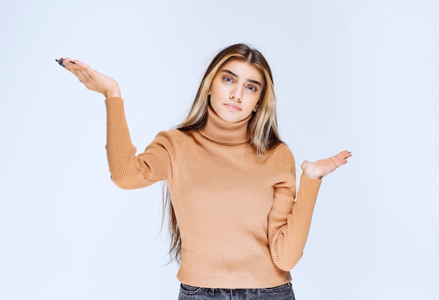 Immagine di un modello di giovane donna in maglione marrone in piedi e alzando le mani.
