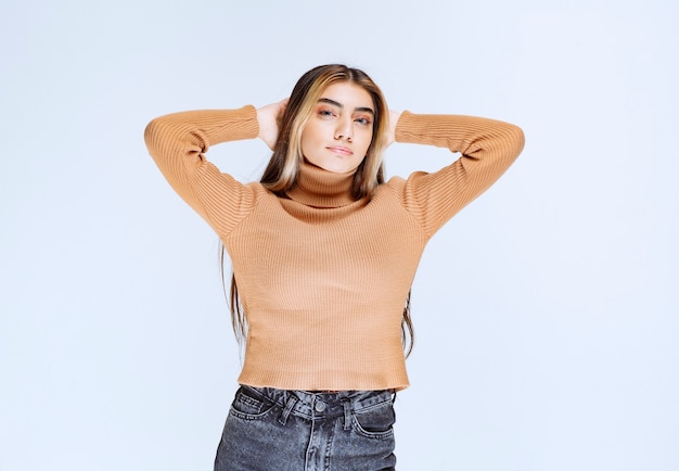 Immagine di un modello di giovane donna in maglione marrone in piedi e tenendosi per mano dietro la testa.