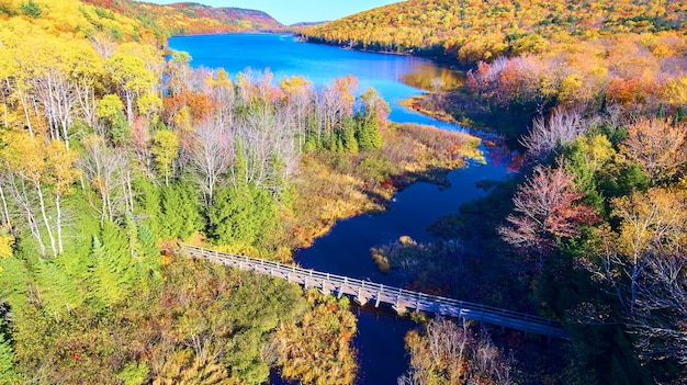 Immagine di un ponte pedonale di legno su un fiume che conduce a un gigante come nelle montagne circondate da una foresta autunnale