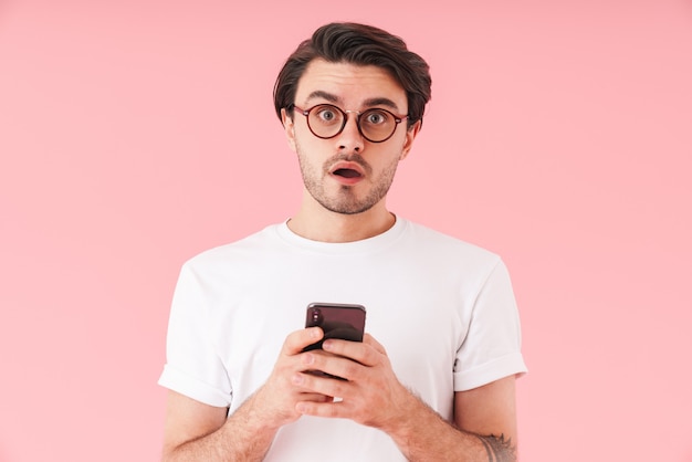 Immagine di un uomo scioccato con la barba lunga che indossa occhiali che guarda e digita sul cellulare isolato