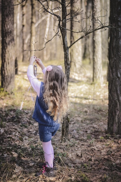 Immagine di una bambina con i capelli lunghi in una fascia che gioca nella foresta