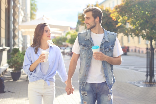 Immagine di una bella coppia felice in abiti estivi che sorride e si tiene per mano insieme mentre cammina per la strada della città