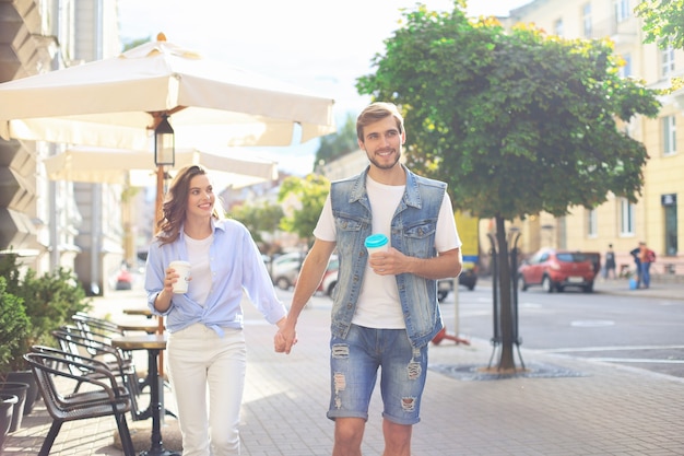 Immagine di una bella coppia felice in abiti estivi che sorridono e si tengono per mano mentre camminano per le strade della città.
