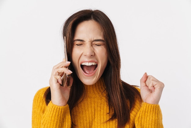 Immagine di una bella donna bruna adulta che indossa un maglione urlando e parlando al cellulare isolato su bianco